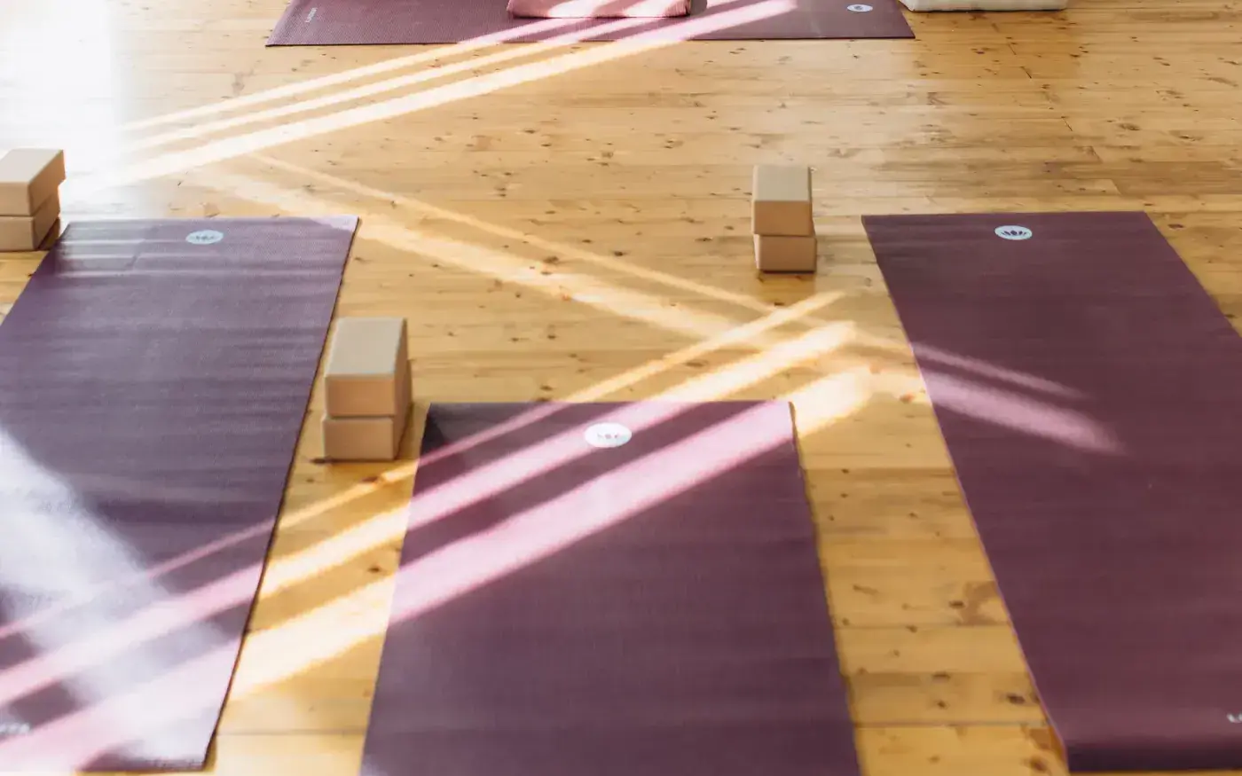 Sonnenlicht auf dem Holzboden und ausgerollte Matten im Yogasalon
